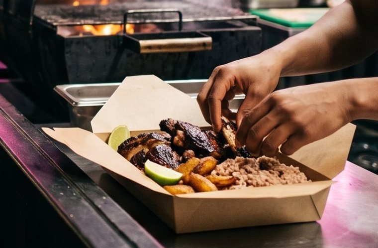 Jerk chicken with rice and peas, fried plantain and lime in a kraft box